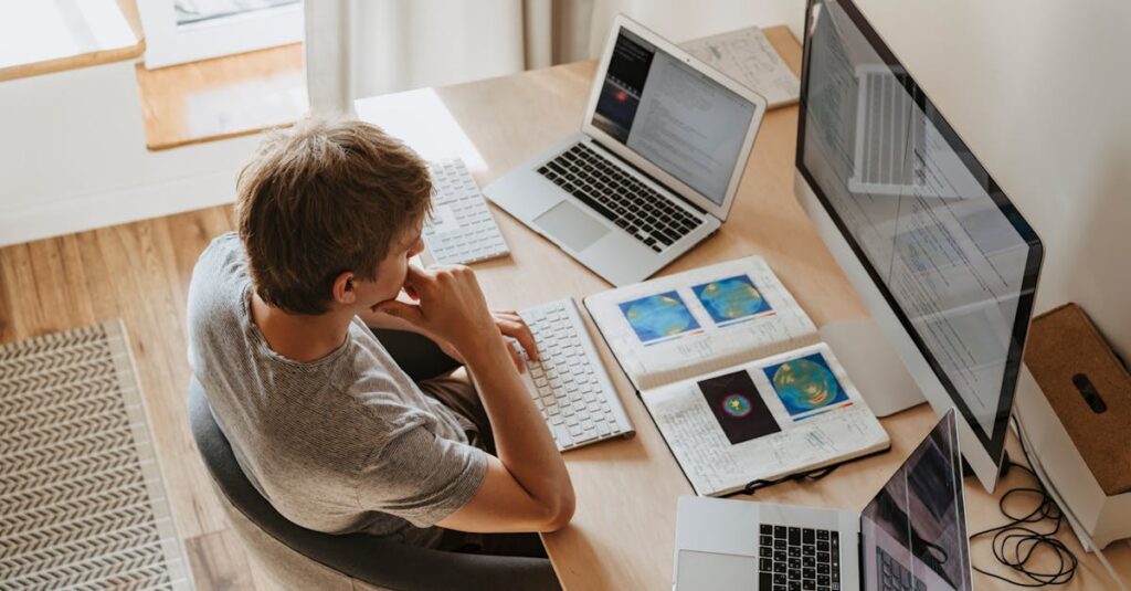 Top view of young programmer working on multiple laptops in a modern office setting.